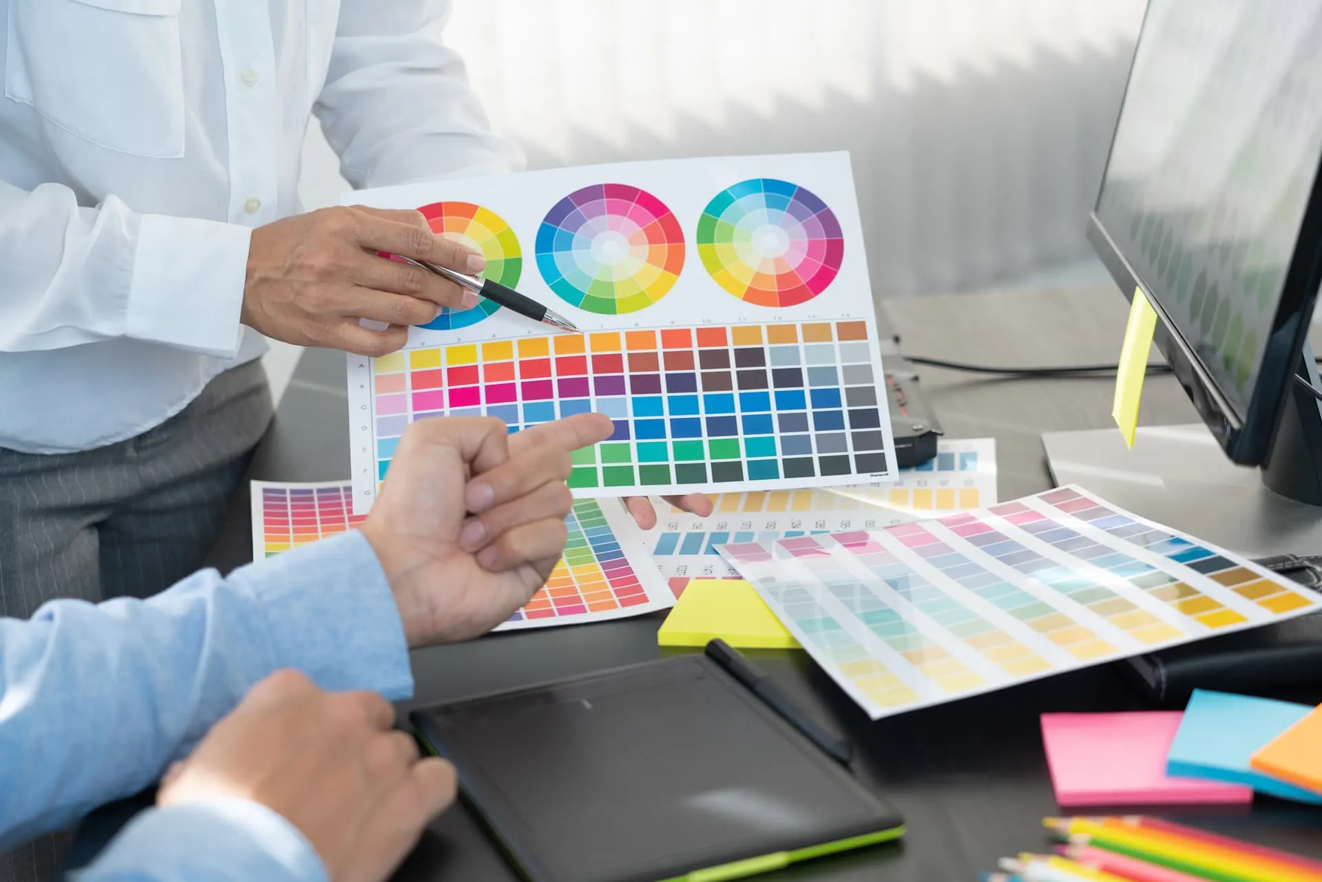 Designer comparing colour swatches and a colour wheel at a computer
